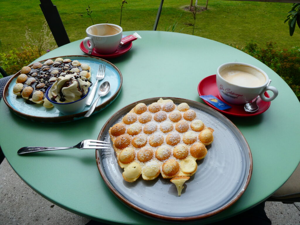 das Bild zeigt einen Tisch mit zwei Kaffeetassen und zwei Tellern mit Waffeln