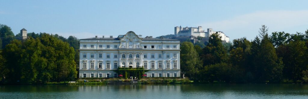 Das Bild zeigt den Leopoldskroner Weiher im Vordergrund, das Hotel Schloß Leopoldskron in der Mitte und die Festung Hohensalzburg im Hintergrund